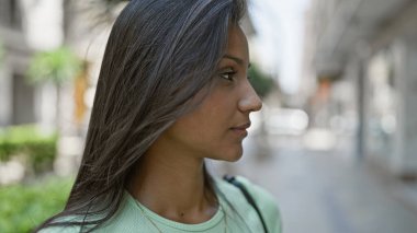 Sokakta ciddi bir ifadeyle yan tarafa bakan genç Latin kadın.