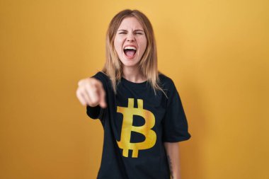 Bitcoin tişörtü giyen sarışın beyaz bir kadın kameraya kızgın ve sinirli olduğunu gösteriyor. 