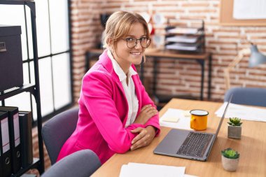 Young blonde girl business worker sitting with arms crossed gesture at office