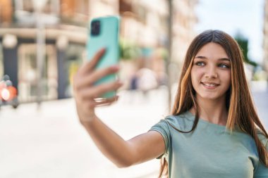 Sevimli kız gülümsüyor. Kendine güveni tam. Sokakta akıllı telefonun yanında özçekim yapıyor.