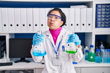 Laboratuvarda çalışan Asyalı genç bir kadın komik suratıyla yanaklarını şişiriyor. Ağzı havayla şişer, havayı yakalar.. 