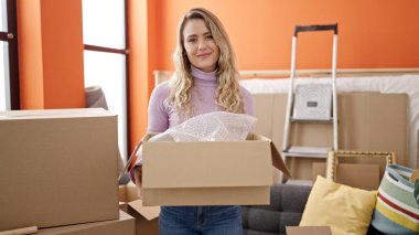 Young blonde woman smiling confident holding package at new home