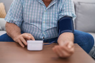 Orta yaşlı, kır saçlı, nabız ölçer kullanan bir adam.