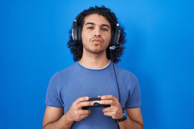 Kıvırcık saçlı, video oyunu oynayan, kameraya bakıp öpüşen tatlı ve seksi İspanyol bir adam. aşk ifadesi. 