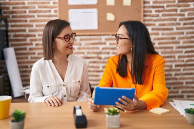 Two women business workers using touchpad working at office