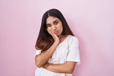 Pembe arka planda duran genç Arap kadın çapraz kollu depresyon sorunlarından yorgun ve sıkılmış göründüğünü düşünüyor.. 