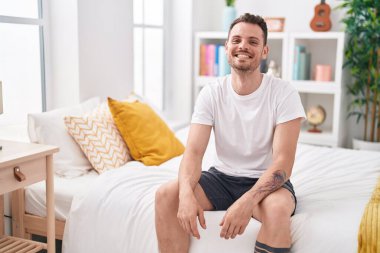 Young hispanic man smiling confident sitting on bed at bedroom