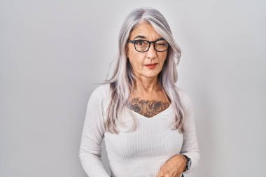 Beyaz arka planda gri saçlı orta yaşlı bir kadın kameraya seksi bir ifadeyle bakıyor, neşeli ve mutlu bir yüzle.. 