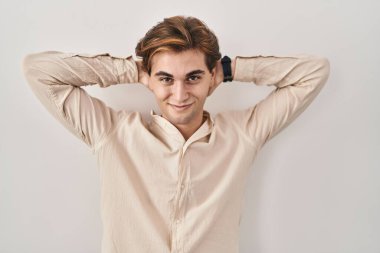 İzole edilmiş arka planda duran genç adam rahatlıyor ve esniyor, kollar ve eller başının ve boynunun arkasında mutlu bir şekilde gülümsüyor. 