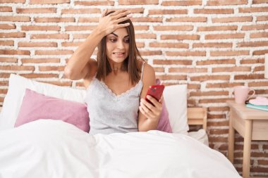 Genç İspanyol kadın akıllı telefon kullanıyor. Evde yatakta oturuyor. Stresli ve sinirli. 