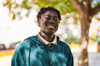 Afro-Amerikalı adam parkta kendine güvenerek gülümsüyor.