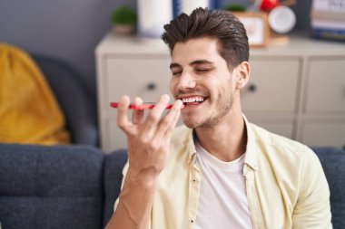 Genç İspanyol adam akıllı telefonda konuşuyor. Evdeki kanepede oturuyor.