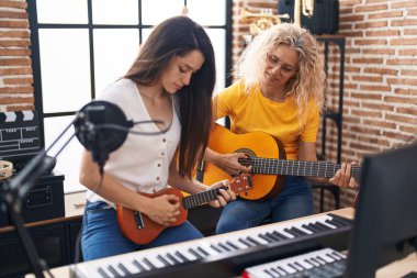 Müzik stüdyosunda klasik gitar ve ukulele çalan iki kadın müzisyen.