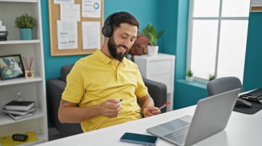 Genç İspanyol iş adamı, ofiste baterist jestleri yaparak müzik dinliyor.