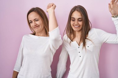 Orta yaşlı anne ve küçük kızı pembe arka planda dans ediyor mutlu ve neşeli, gülümsüyor rahat ve kendinden emin bir şekilde müzik dinliyor. 