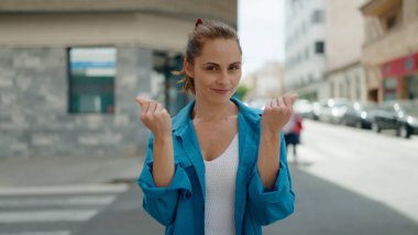 Young woman smiling confident doing spend money gesture at street