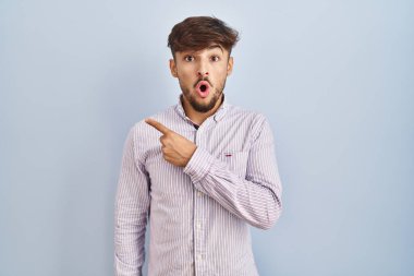 Mavi arka planda duran sakallı bir Arap parmağını yana uzatıp, ağzı açık şaşkın bir ifadeyle şaşırdı.. 