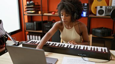 Müzik stüdyosunda dizüstü bilgisayar kullanarak piyano çalan Afrikalı Amerikalı kadın müzisyen.