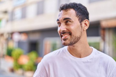 Young hispanic man smiling confident looking to the side at street