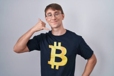 Bitcoin t-shirt giyen beyaz sarışın adam telefonla el ve parmak hareketleriyle gülümsüyor telefonda konuşuyor gibi. iletişim kavramları. 