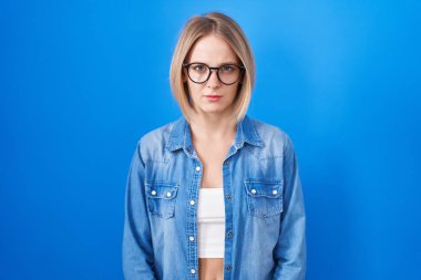 Mavi arka planda duran genç beyaz kadın şüpheci ve gergin, sorun yüzünden surat asıyor. negatif kişi. 