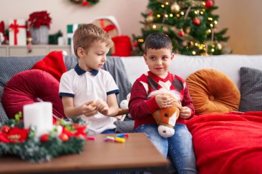 İki çocuk evdeki Noel ağacının yanında kanepede oyuncaklarla oynuyor.