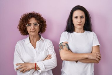 Hispanic mother and daughter wearing casual white t shirt over pink background skeptic and nervous, disapproving expression on face with crossed arms. negative person. 