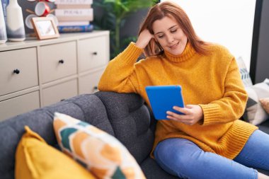 Young beautiful plus size woman using touchpad sitting on sofa at home