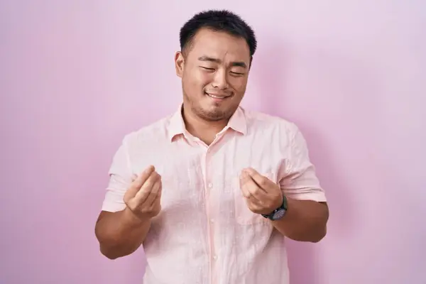 Китайский Молодой Человек Стоящий Розовом Фоне Делает Денежный Жест Руками — стоковое фото