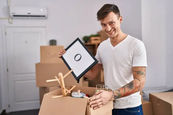 Young man smiling confident unpacking cardboard box at new home