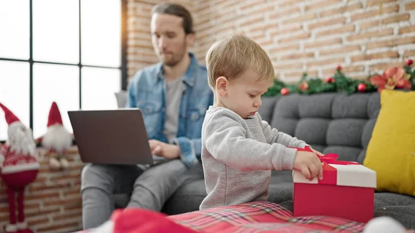 Father and son unpacking christmas gift using laptop at home