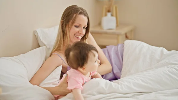 Mother and daughter sitting on bed smiling at bedroom