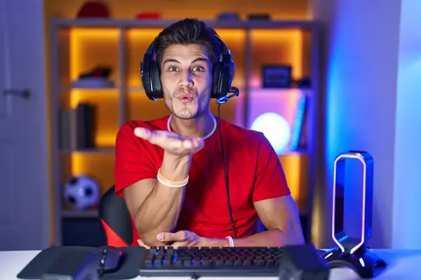 Young hispanic man playing video games looking at the camera blowing a kiss with hand on air being lovely and sexy. love expression.