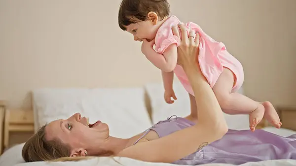 Mother and daughter lying on bed holding baby on air at bedroom