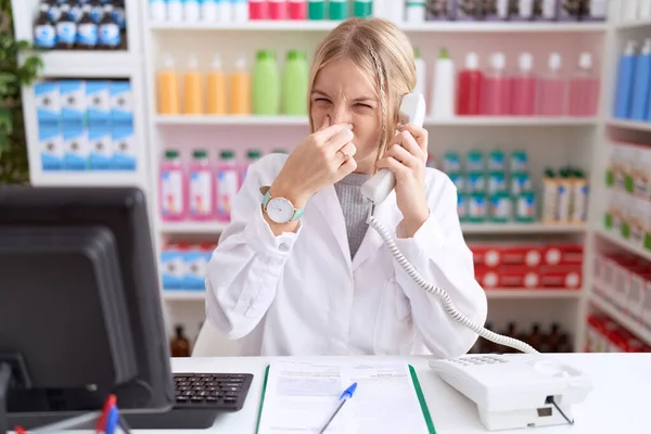 薬局のドラッグストアで働く若い白人女性は 電話で臭いと嫌な 耐え難い臭いを嗅ぎ 鼻に指で息を止めている 悪い匂いがする — ストック写真