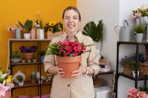Joven Mujer Caucásica Trabajando Floristería Sosteniendo Maceta Sacando Lengua Feliz —  Fotos de Stock