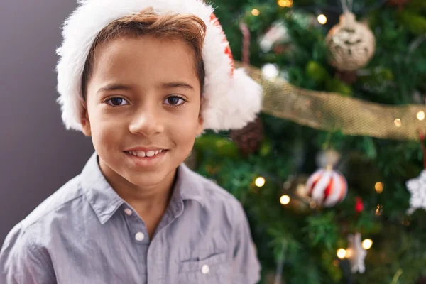 自宅でクリスマスツリーに立って自信を持って微笑む愛らしいヒスパニックの少年 — ストック写真