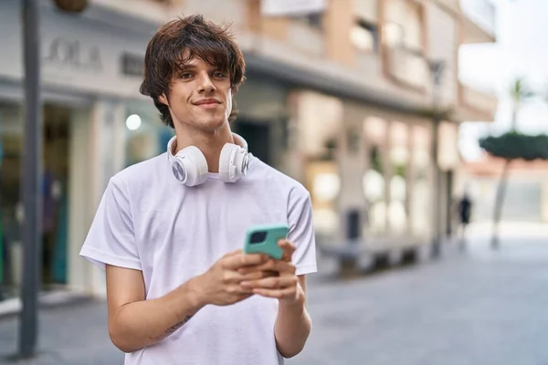 Young blond man smiling confident using smartphone at street