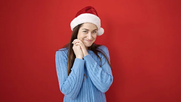 年轻的高加索女人带着自信的笑容 戴着圣诞帽 披着孤零零的红色背景 — 图库照片