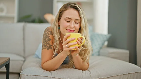 Young Blonde Woman Smelling Cup Coffee Lying Sofa Home — Stock Photo, Image