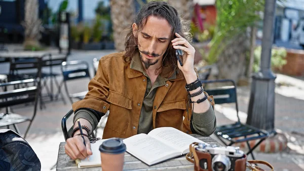 年轻的他的惊慌失措的游客坐在桌子上用智能手机聊天 在咖啡店的阳台上记笔记 — 图库照片