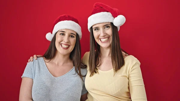 Dvě Ženy Objímající Navzájem Nosit Vánoční Klobouk Přes Izolované Červené — Stock fotografie