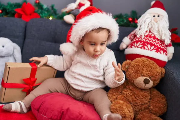 自宅でソファーに座っているクリスマスの帽子をかぶっている愛らしいヒスパニックの幼児 — ストック写真