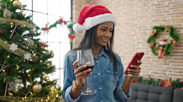 African american woman using smartphone drinking wine celebrating christmas at home