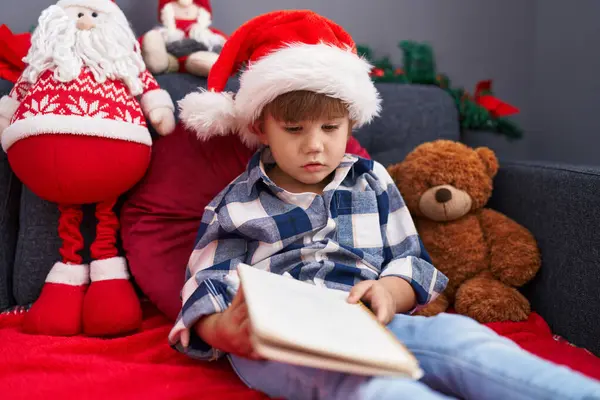 他那可敬的惊慌失措的孩子坐在沙发上看书 坐在家里的圣诞装饰品旁 — 图库照片