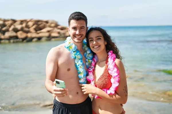 Young Hispanic Couple Tourists Wearing Hawaiian Lei Using Smartphone Seaside — Stock Photo, Image