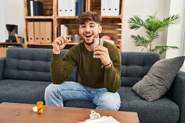 Arab man with beard working on depression holding pills and water smiling and laughing hard out loud because funny crazy joke.