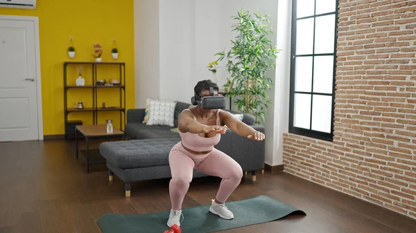 African american woman training legs exercise using virtual reality glasses at home