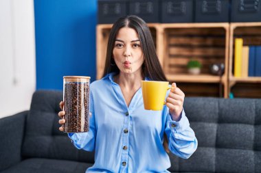 Genç esmer kadın elinde kahve çekirdekleri ve bir fincan kahve ile balık suratlı ve şaşı gözlü çılgın ve komik.. 