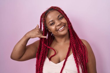 Pembe arka planda örülü saçları olan Afro-Amerikalı kadın telefonla el ve parmak hareketleriyle gülümsüyor telefonda konuşuyor gibi. iletişim kavramları. 
